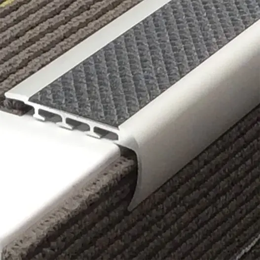 An aluminum safety stair nosing trim with a textured grey anti-slip rubber insert installed on a ribbed carpet step.